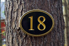 Oval house number with rope border and number with up to four digits painted black and gold.