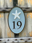 Oval house number painted in three colors and starfish carved on it.