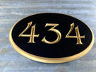 Oval shaped house number sign with 434 carved on it painted black and gold