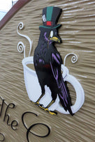 Close of up crow artwork carved on ornate shaped coffee shop sign with business name