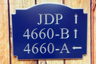 Neighborhood house number sign with multiple numbers and directional arrows carved on it painted blue and silver