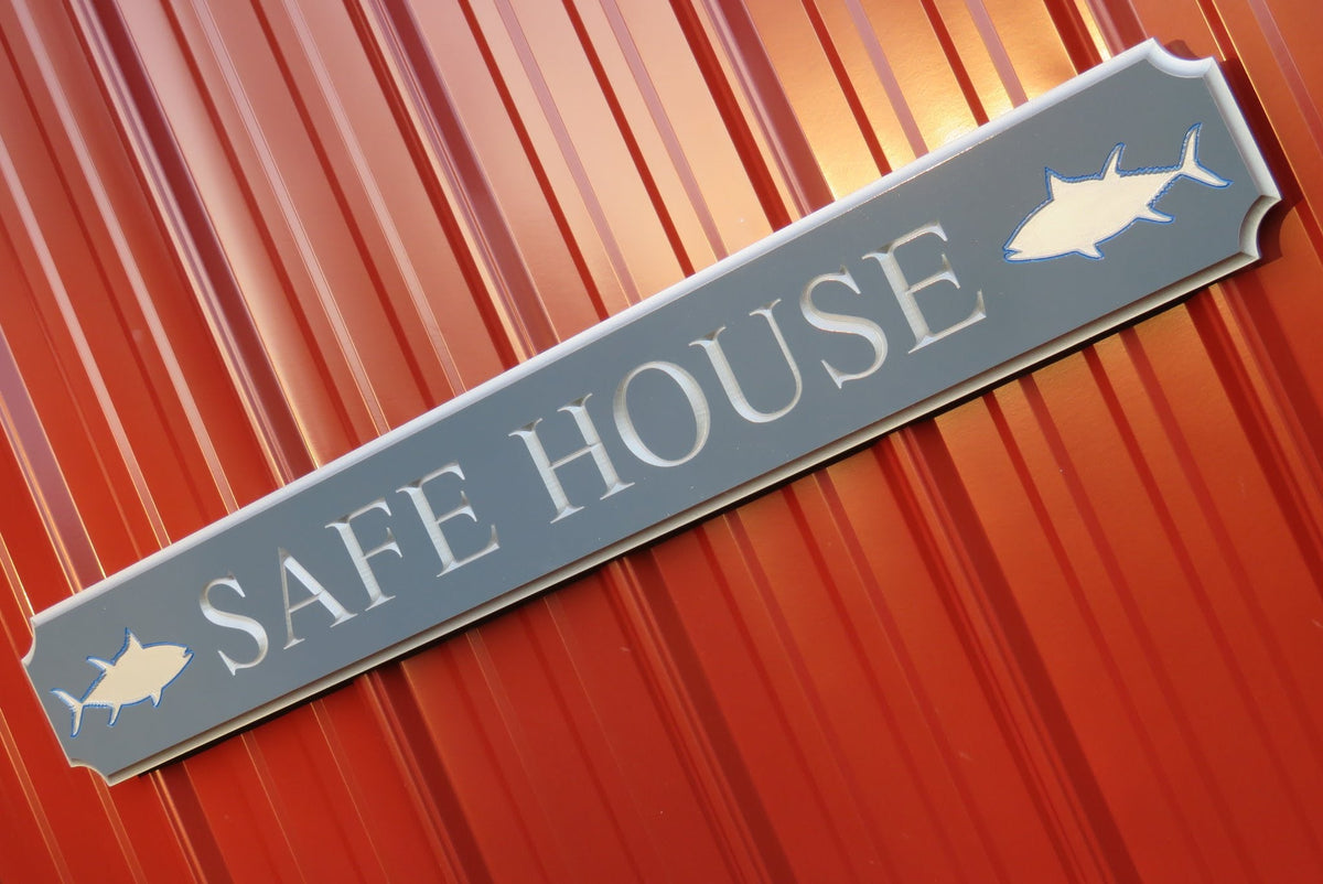 Quarterboard sign with Safe House and sharks carved on it painted grey and silver