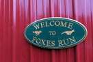 Green and gold painted neighborhood welcome sign with fox and dog carved on it