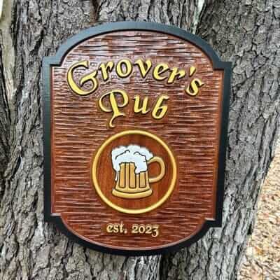 Carved wooden sign reading Grover's Pub, established 2023, with a painted mug of beer, mounted on a tree