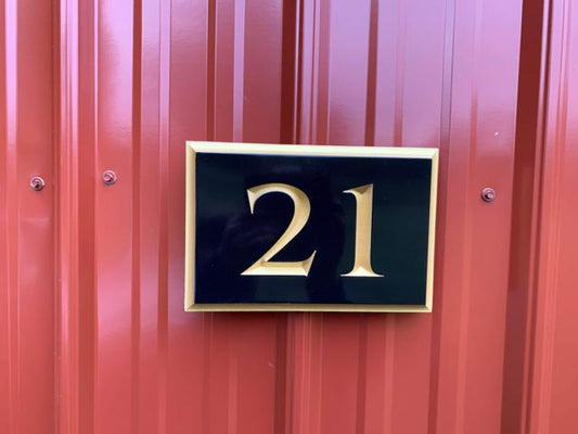 Rectangle shaped house number sign with 21 carved on it painted black and gold