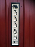 Vertical house number sign with bear and arrow painted cream and black.