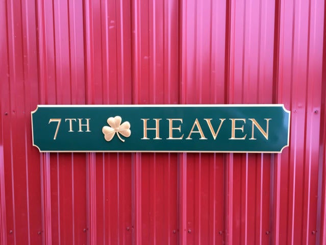 Green and gold quarterboard sign with 7th Heaven carved on it and 3D shamrock mounted on barn