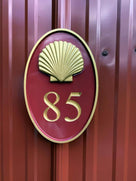 Oval house number painted red and gold with number 85 and realistic scallop shell