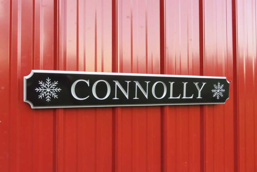 Carved quarterboard sign with last name Connolly and snowflakes on either end carved on it painted black and silver