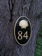 Oval house number painted black and gold with number 84 and realistic scallop shell