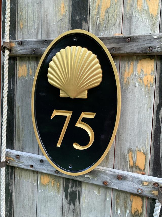 Oval house number painted black and gold with number 75 and realistic scallop shell
