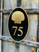 Oval house number painted black and gold with number 75 and realistic scallop shell