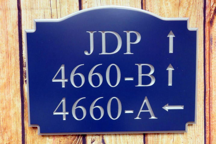 Neighborhood house number sign with multiple numbers and directional arrows carved on it painted blue and silver