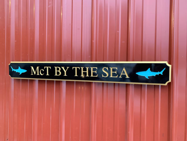Quarterboard with McT by the Sea carved on it and sharks carved on it painted black and gold