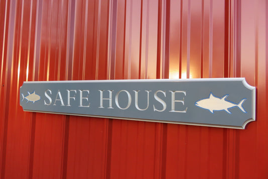 Quarterboard sign with Safe House and sharks carved on it