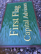 Side view of Rectangular shape company sign painted green, brown, and gold with First Flag Capital Advisors carved on it
