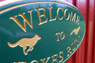 Close up up Green and gold painted neighborhood welcome sign with fox and dog carved on it